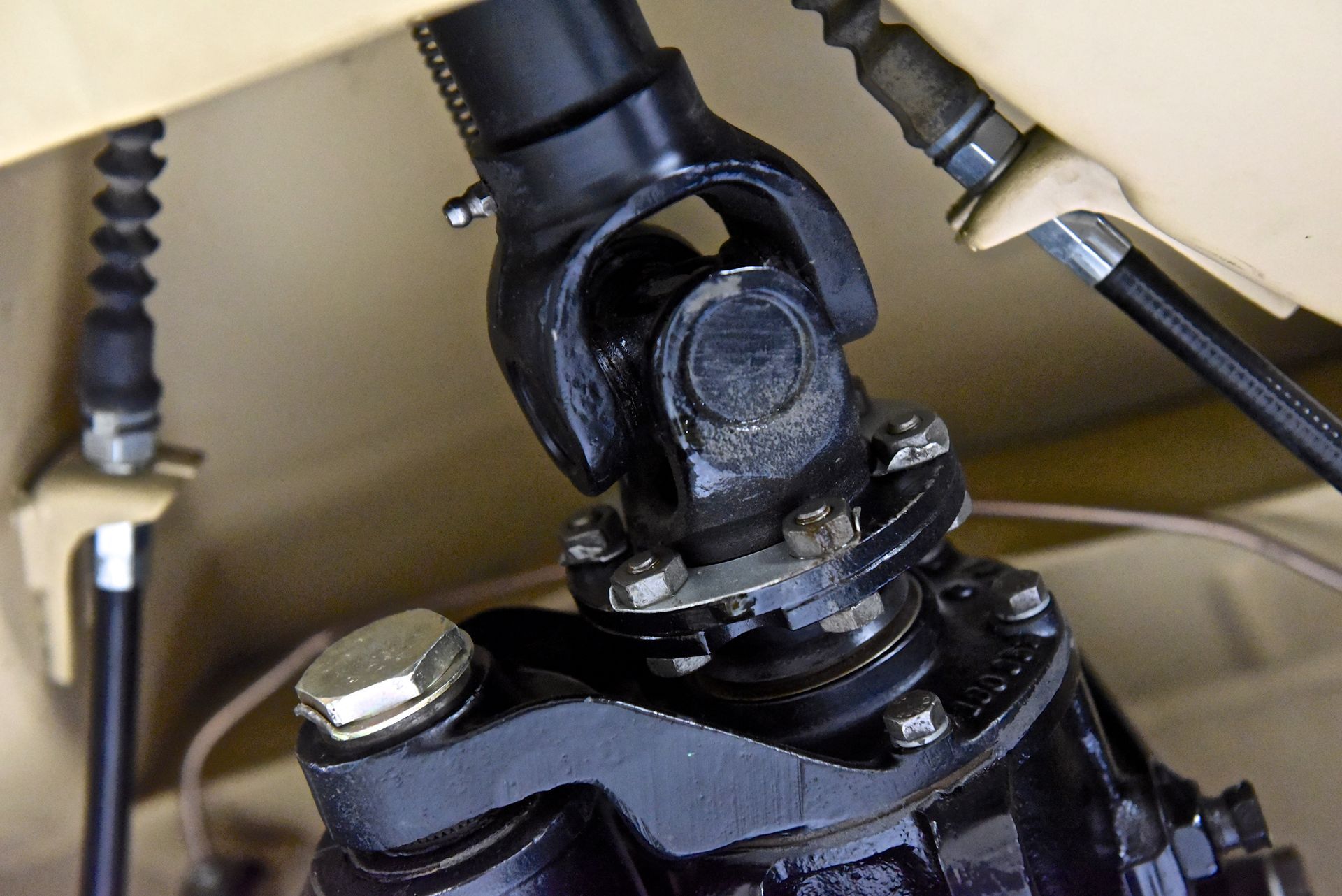 Black U-joint connects two black vehicle components, with associated cables and bolts.