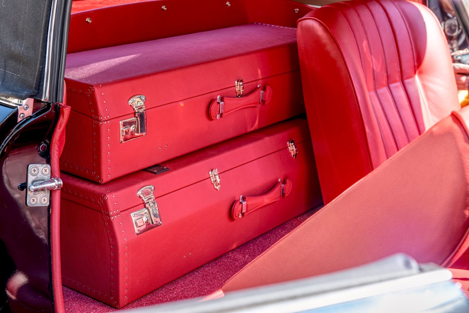 Red vintage suitcases stacked in a car trunk, next to a red car seat.