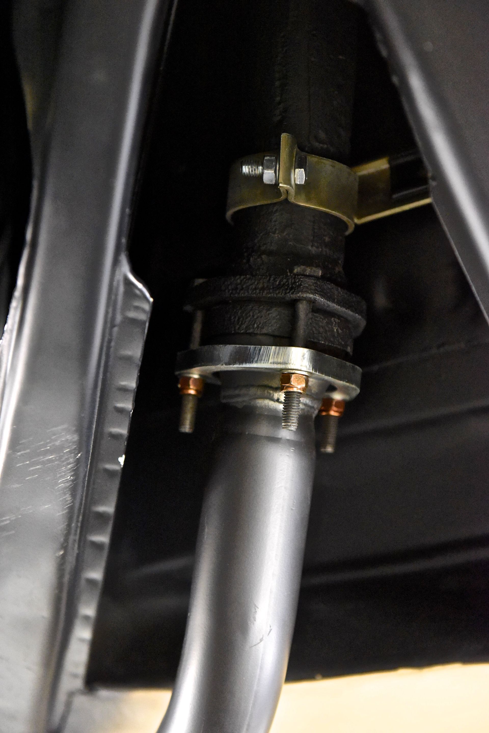 Exhaust pipe connection under a vehicle. Gray metal pipes, black coupling, gold bracket, and orange fasteners.
