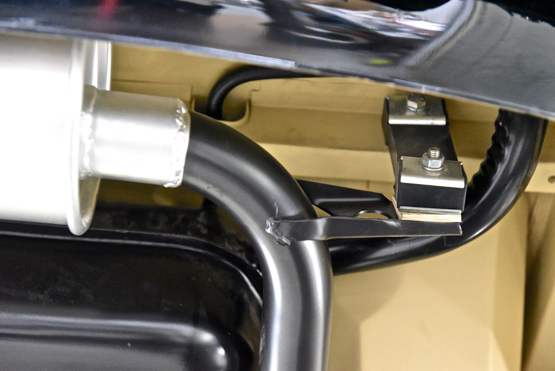 Exhaust pipe and muffler mounted under a car; black and silver against beige chassis.