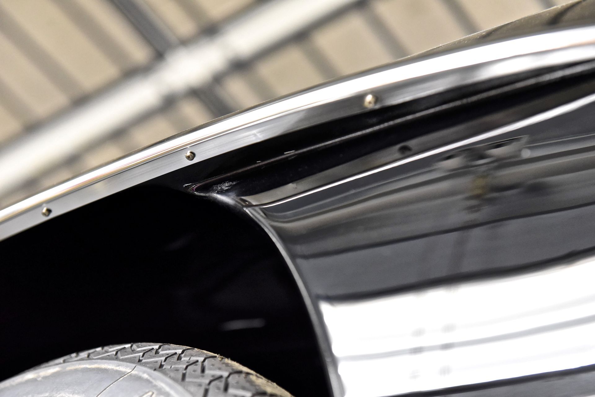 Close-up of a shiny black car fender with chrome trim, partially showing the tire.