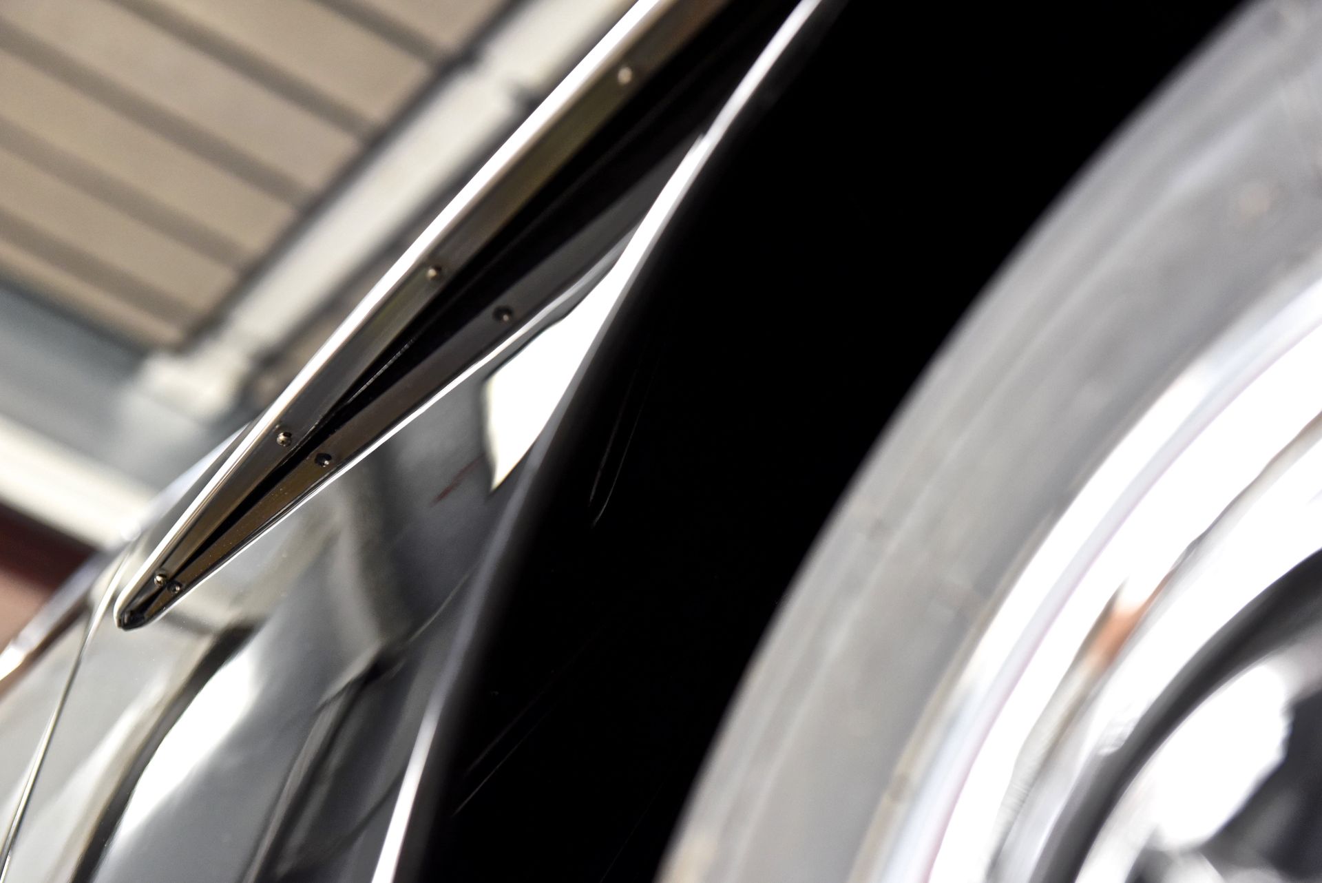 Close-up of a shiny, black car fender with chrome trim and a tire.