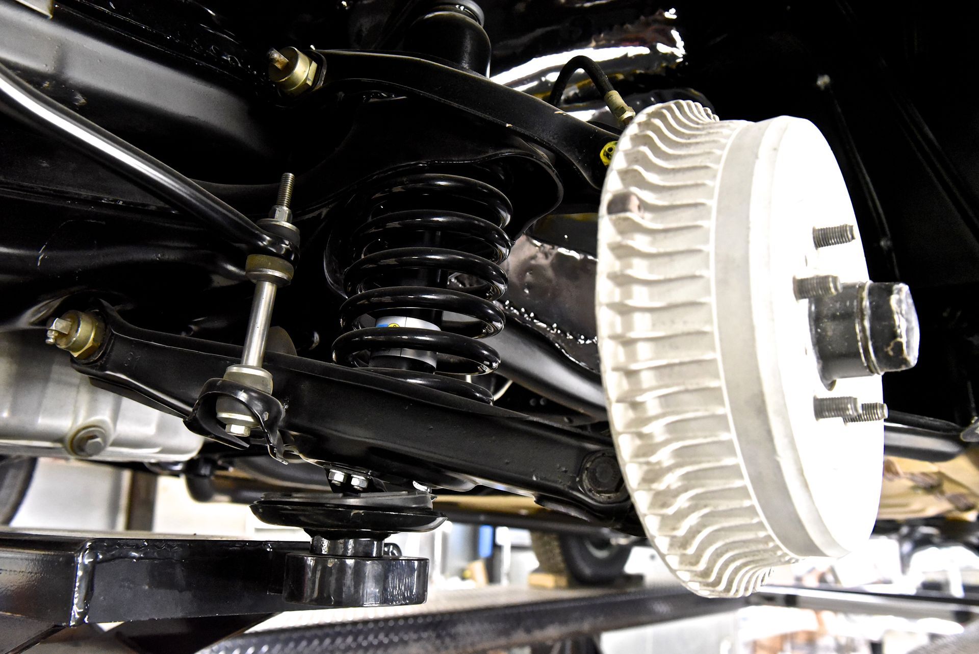 Black car suspension system components, including a coil spring, drum brake, and control arms.