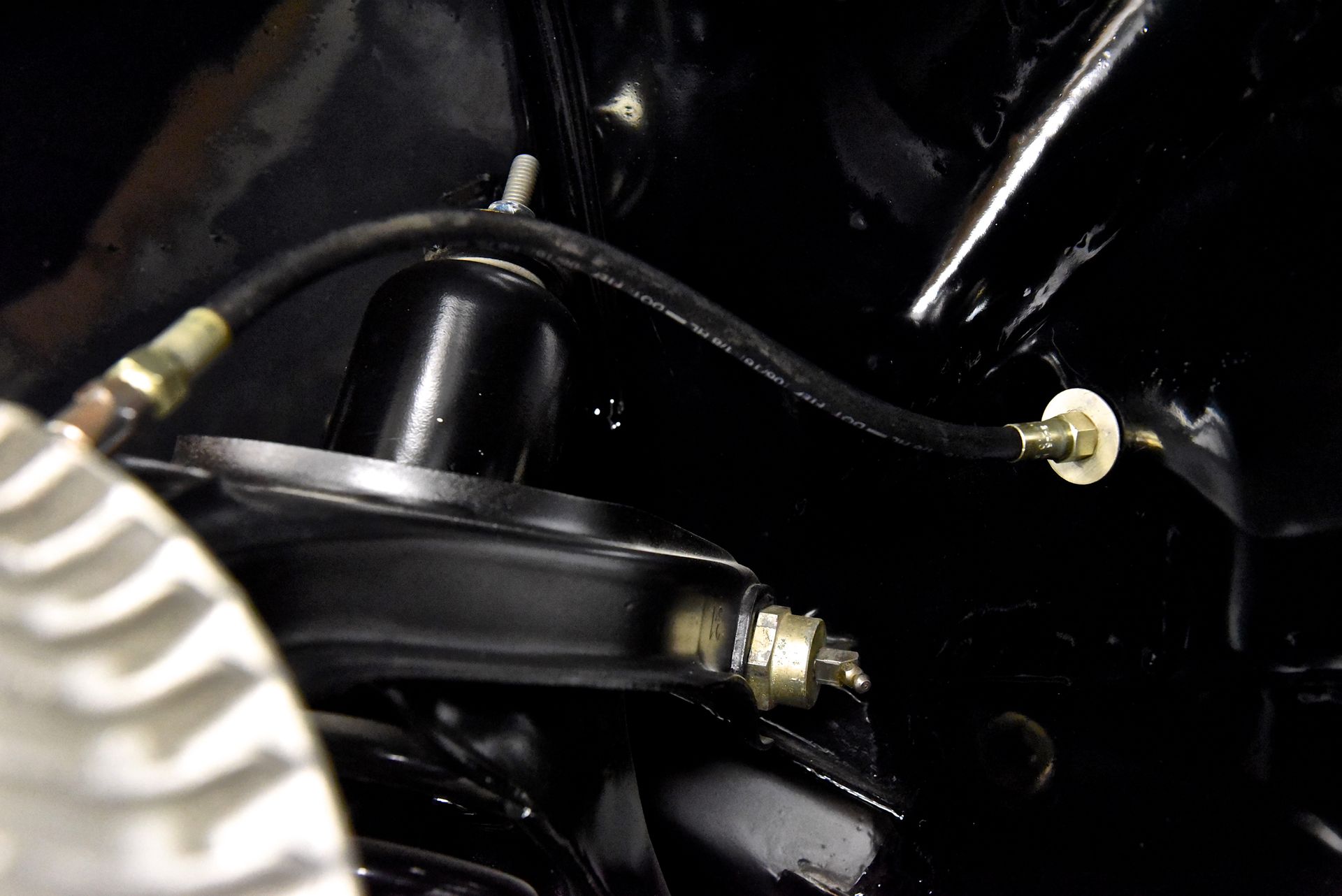 Black car part with a hose and a black strut mount against a black background.