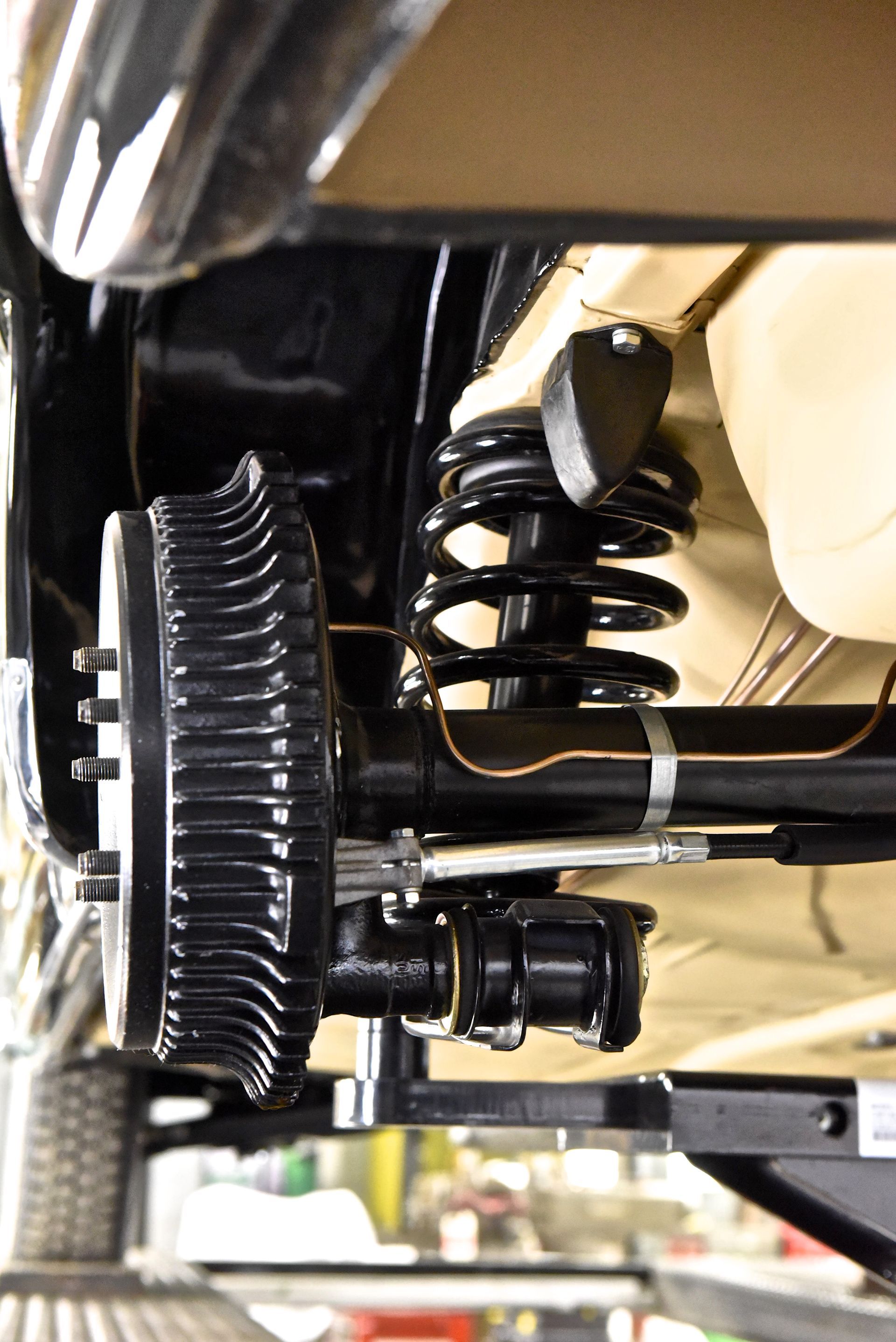 Black car rear suspension: axle, brake drum, spring, shock absorber, and undercarriage.