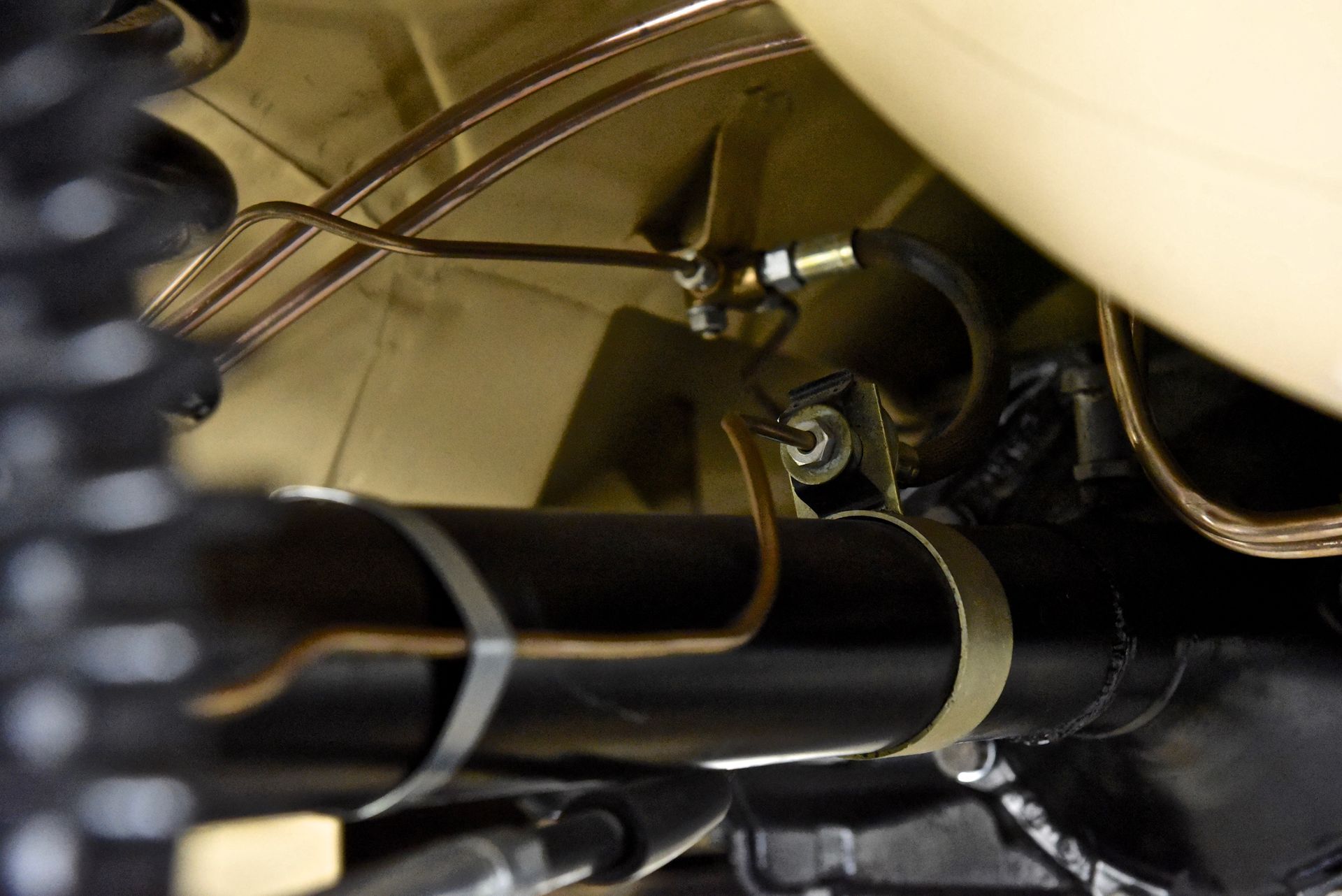 Underside of a vehicle. Brake lines and fittings visible. Brown and black components against a tan background.