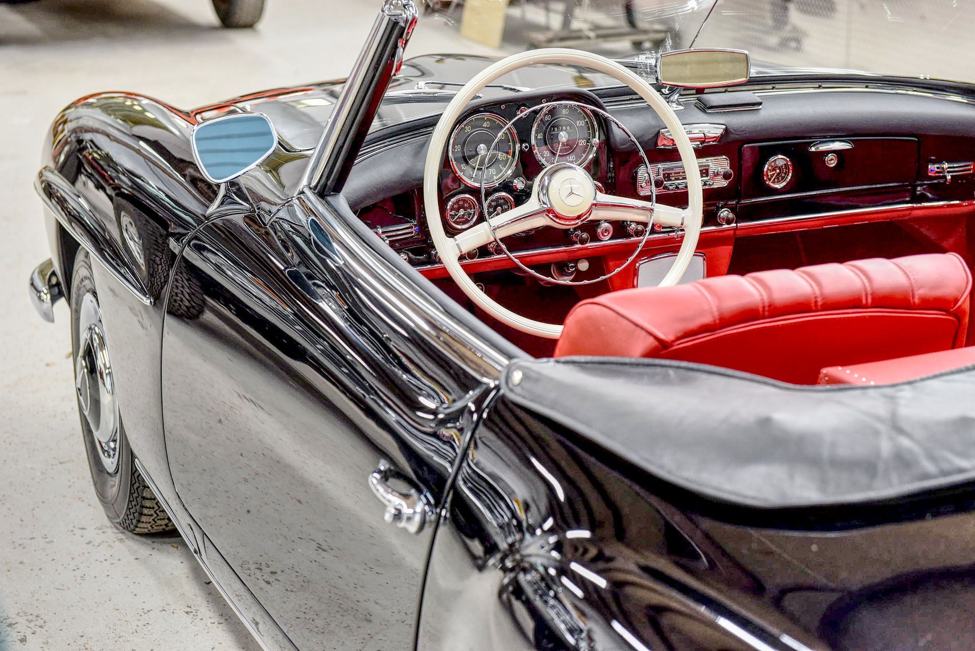 Black vintage convertible car interior with red seats and white steering wheel.