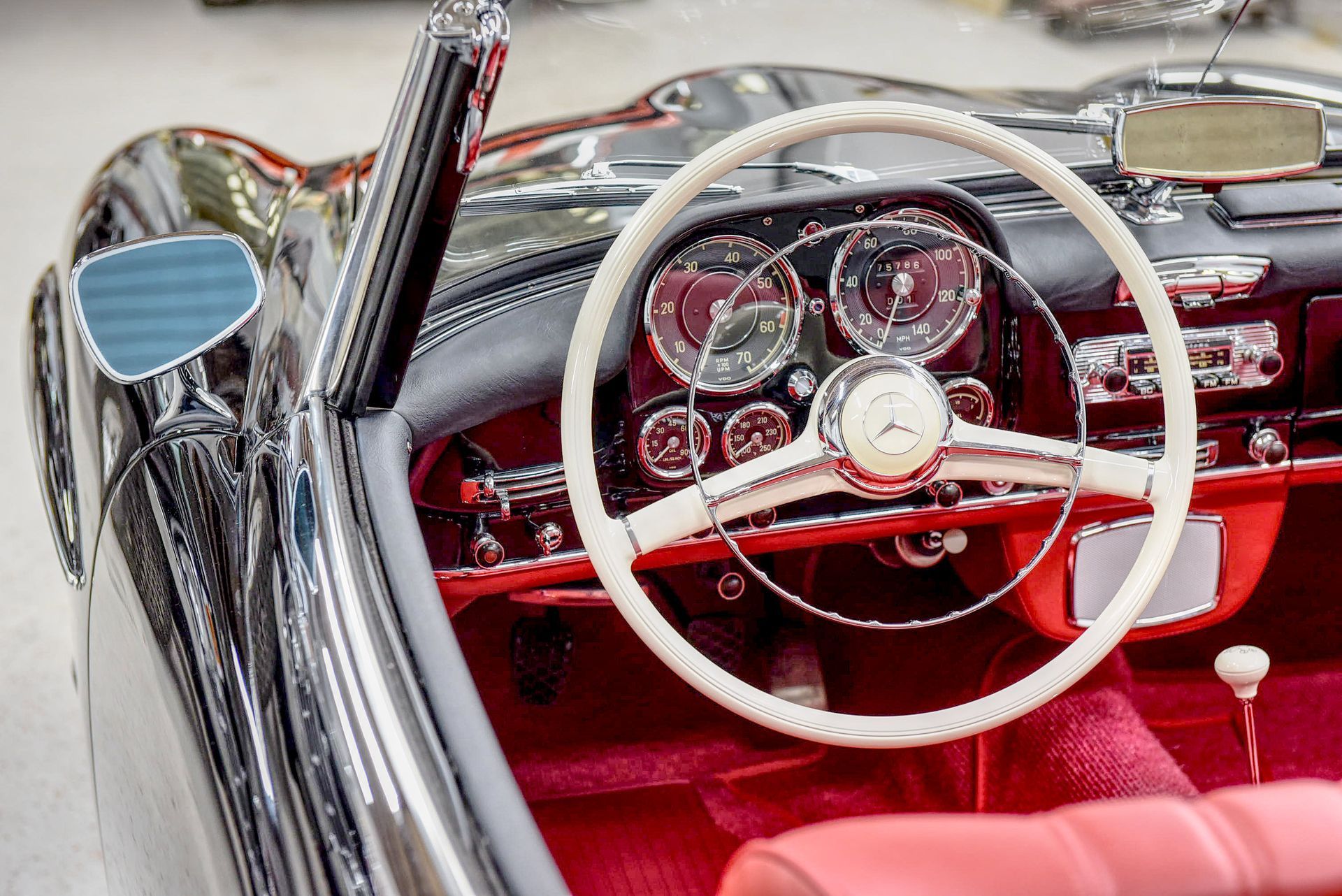Interior view of a classic black convertible car with a red interior, white steering wheel and dashboard gauges.