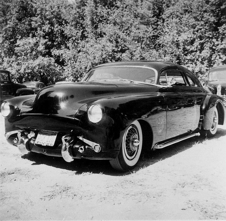 Black vintage custom car with white wall tires parked outdoors.