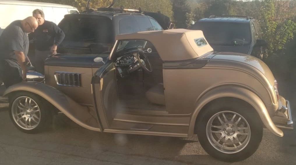Golden convertible hot rod with men examining it.
