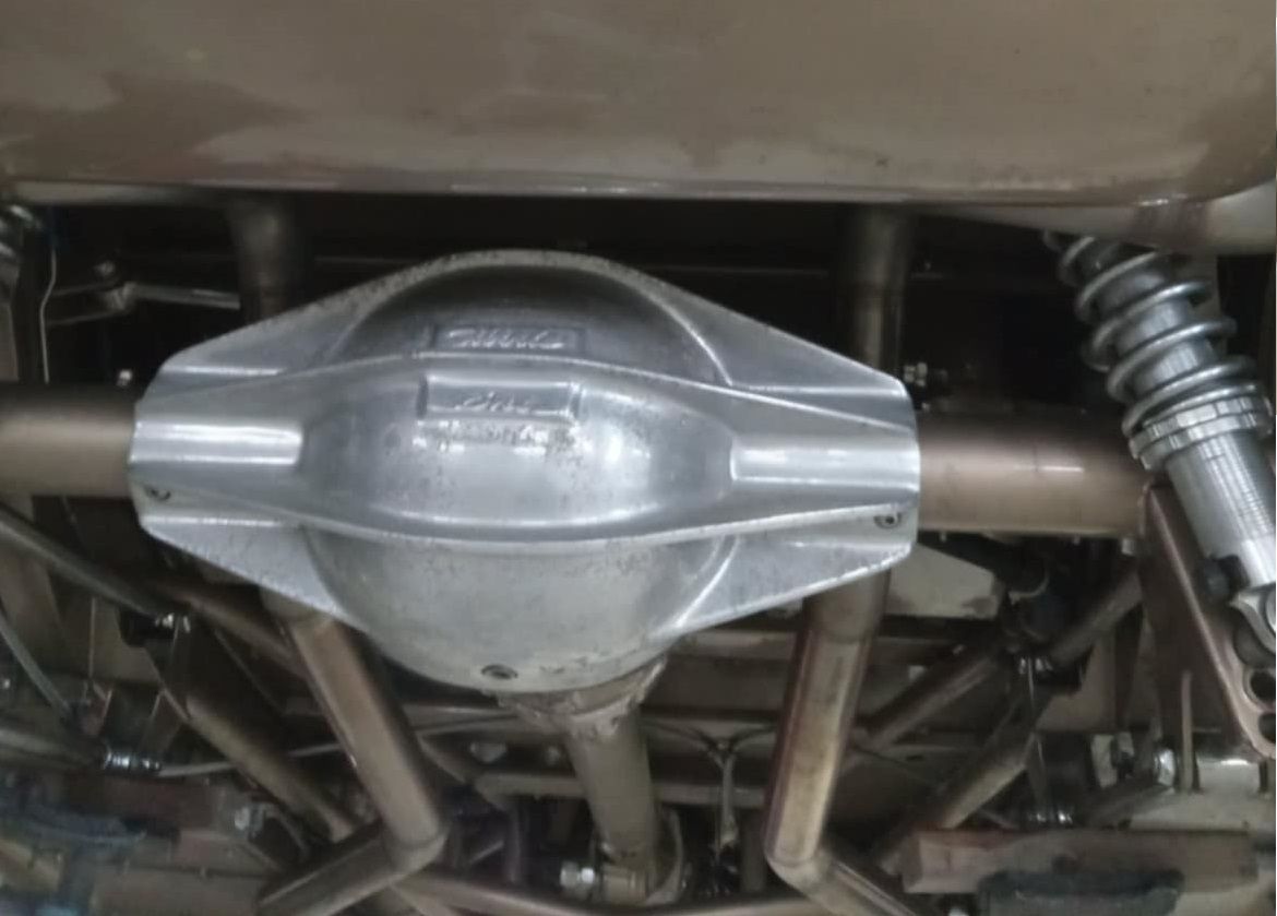 Underside of a car showing a silver differential housing, gold-colored tubes, and coil-over shocks.