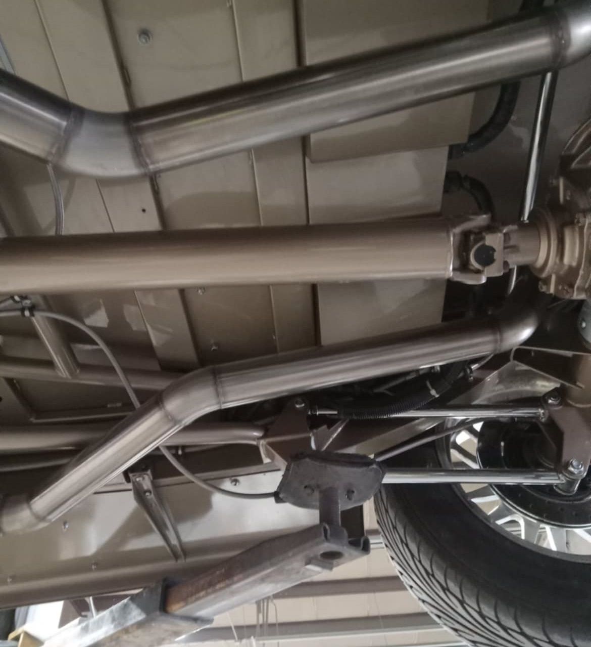 Undercarriage of a vehicle with a stainless steel exhaust system and driveshaft, seen from below.
