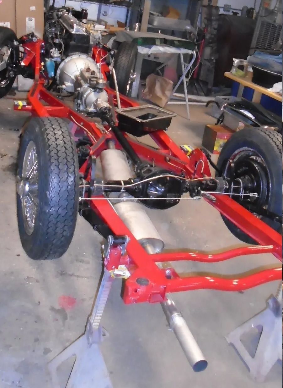 Red chassis of a classic car, tires mounted, supported by jack stands in a garage.