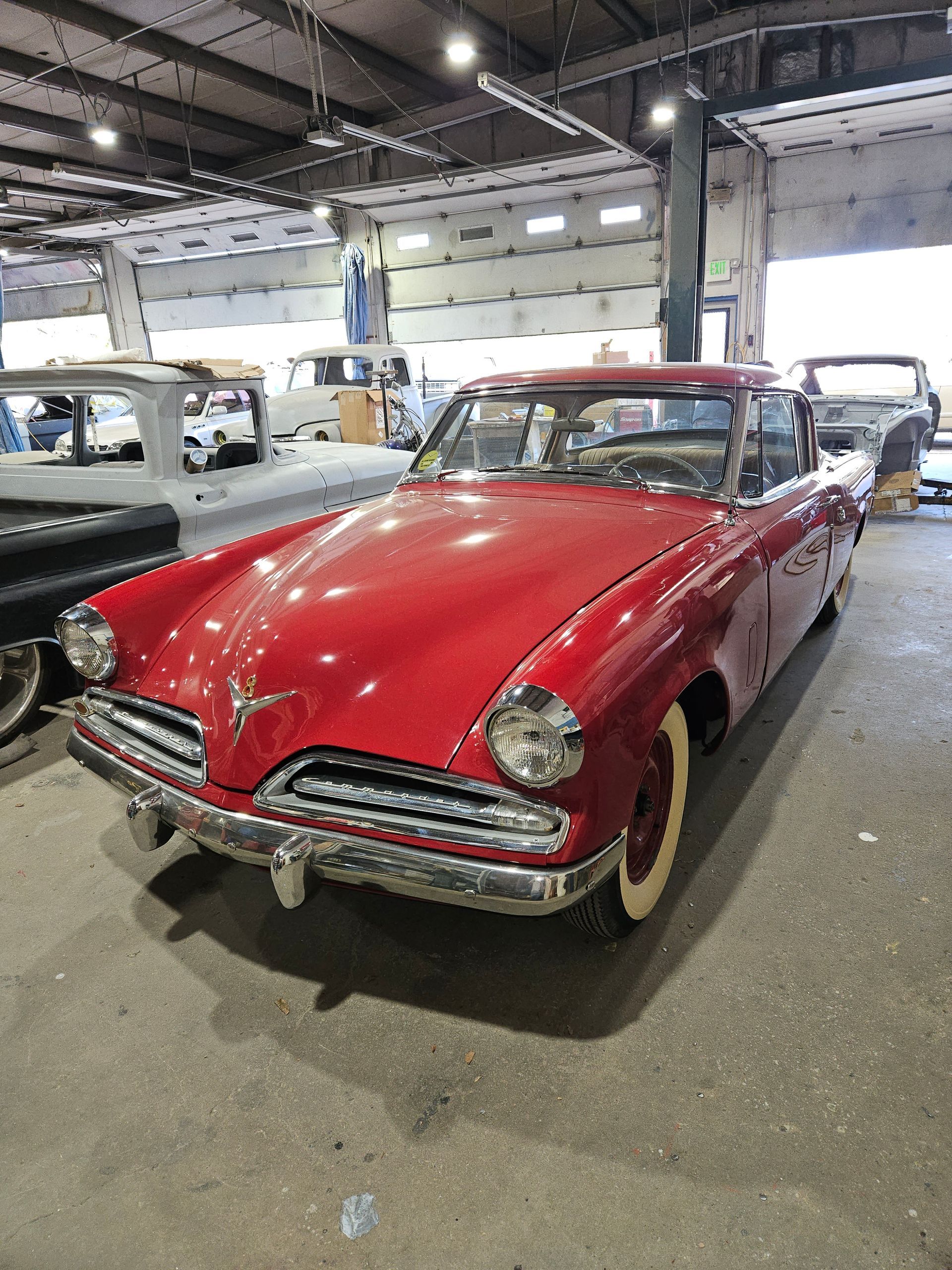 Red classic Studebaker coupe in a repair shop, with whitewall tires, chrome trim.