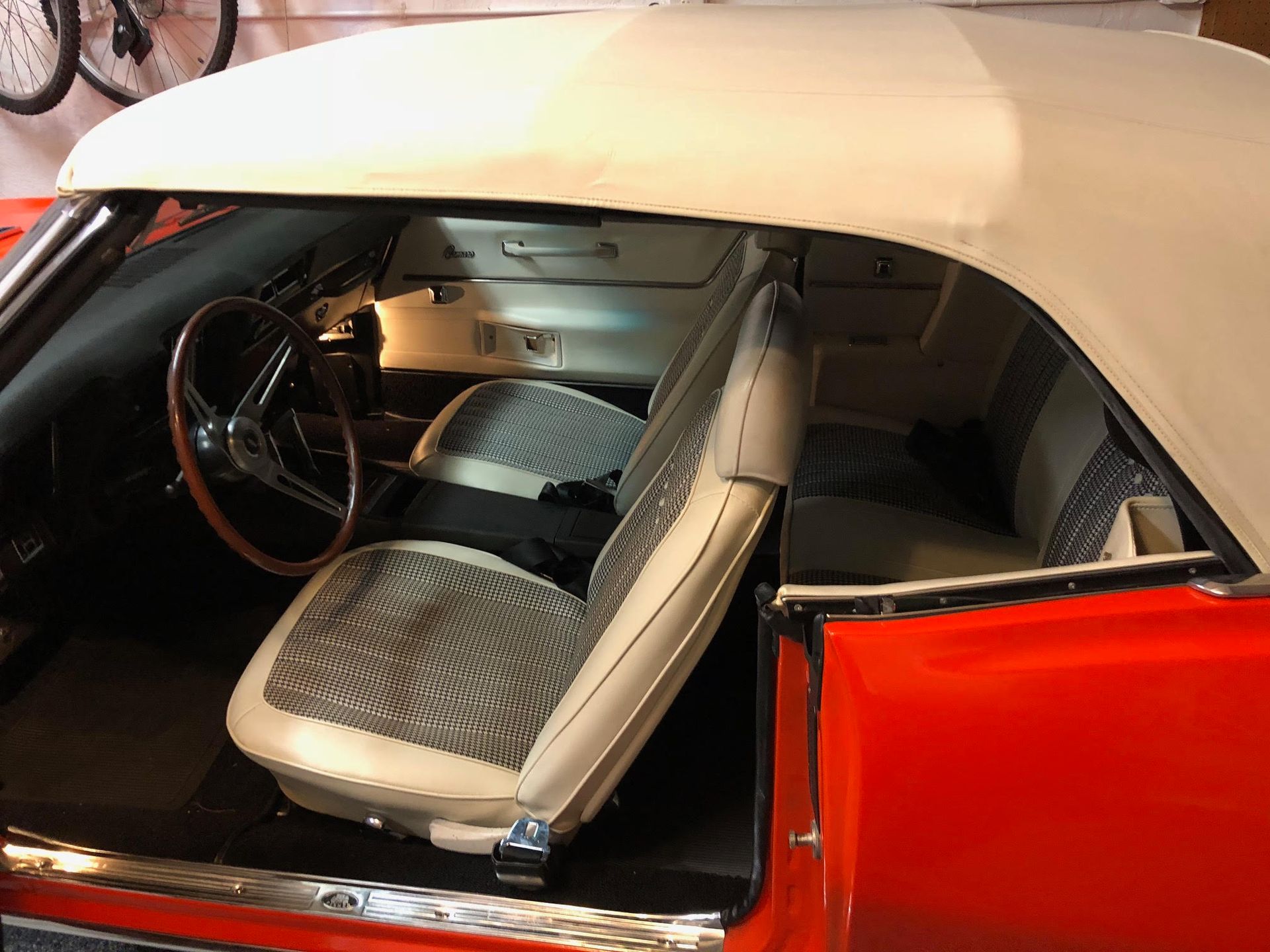 Interior of a classic orange convertible car with cream seats and white convertible top.