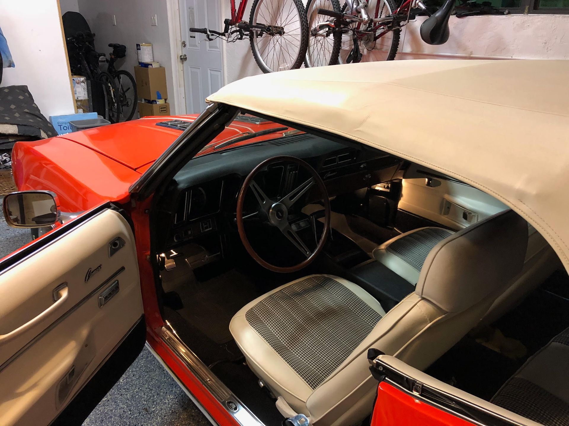 Orange classic car interior with off-white convertible top, seats, and open door. Steering wheel visible.