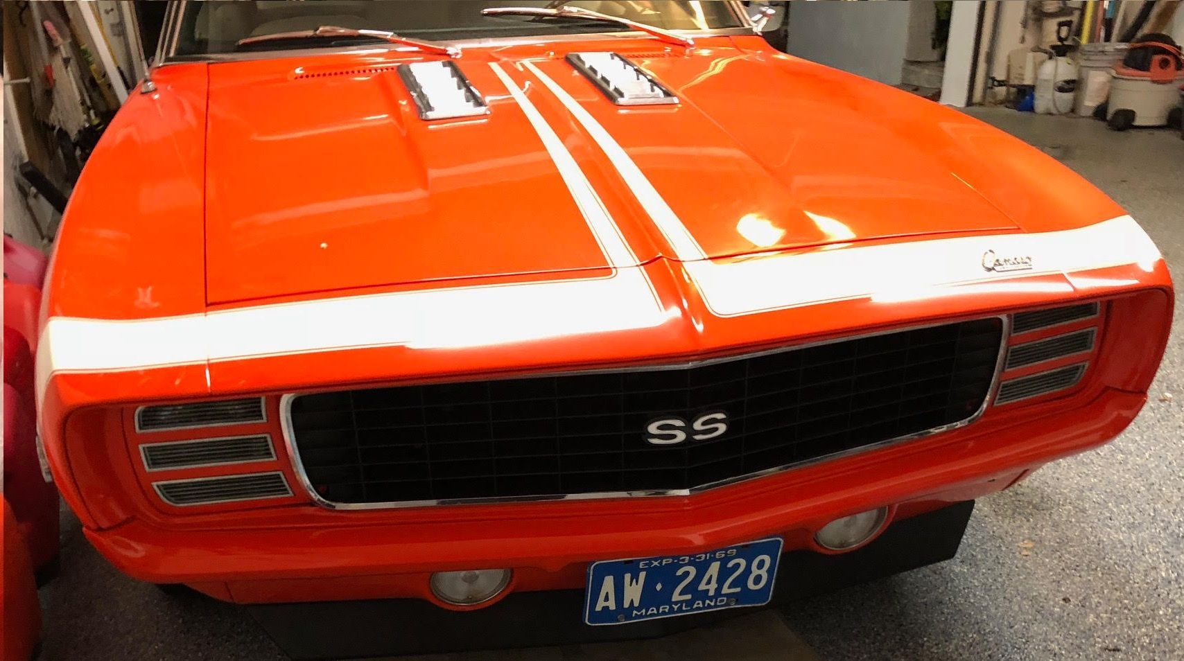 Bright orange classic Chevrolet Camaro SS with white racing stripes on its hood.