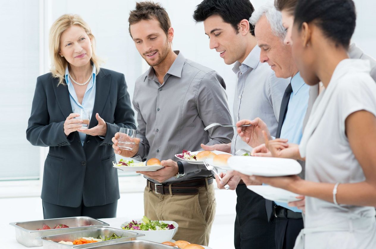 a group of people are standing around a table with plates of food