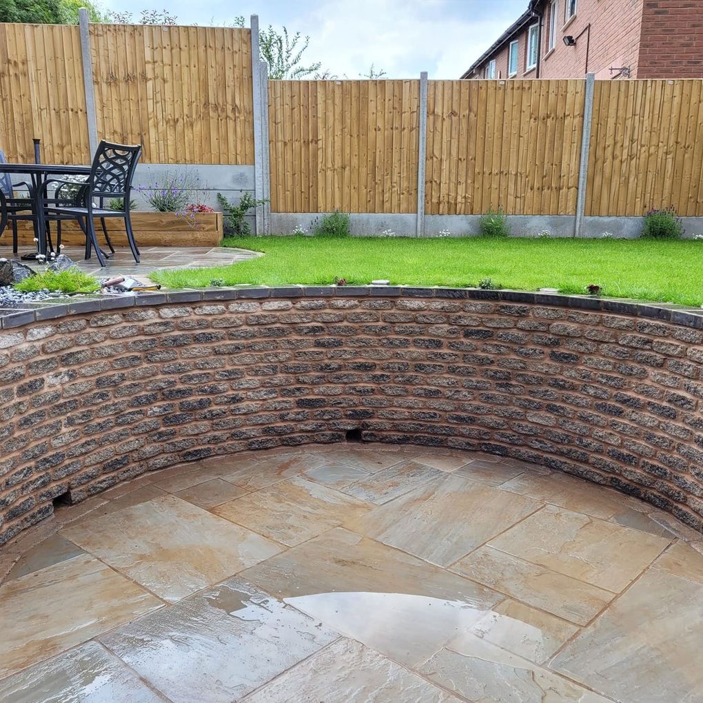 Curved stone-effect retaining wall with weep holes along the base, wrapped round a sandstone circle patio