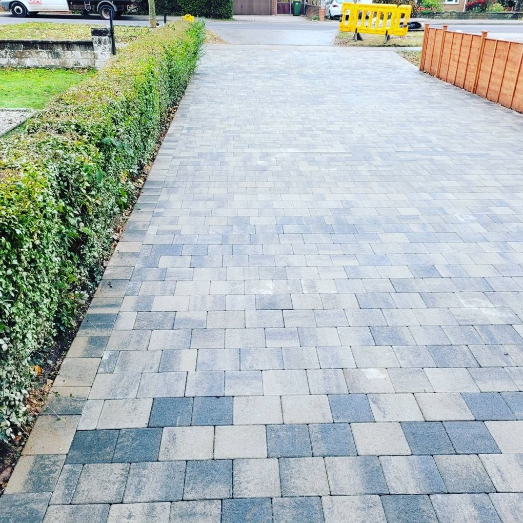 Long grey multi-tone block paving driveway beside a hedge