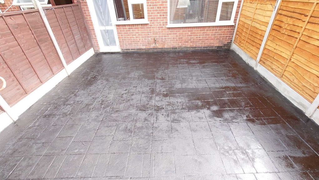 Imprinted concrete driveway in a slate-effect pattern between fences in front of a house