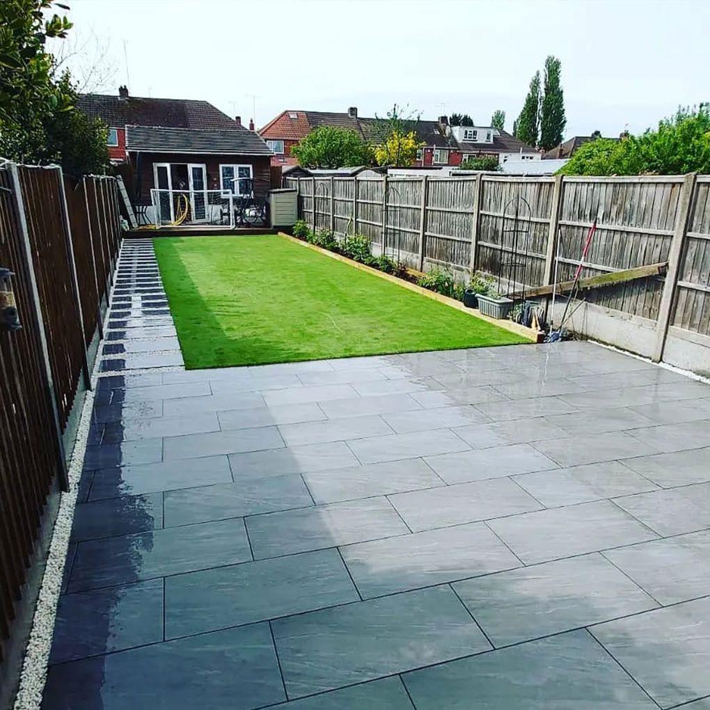 Grey paving patio with a dark border leading on to a long new lawn