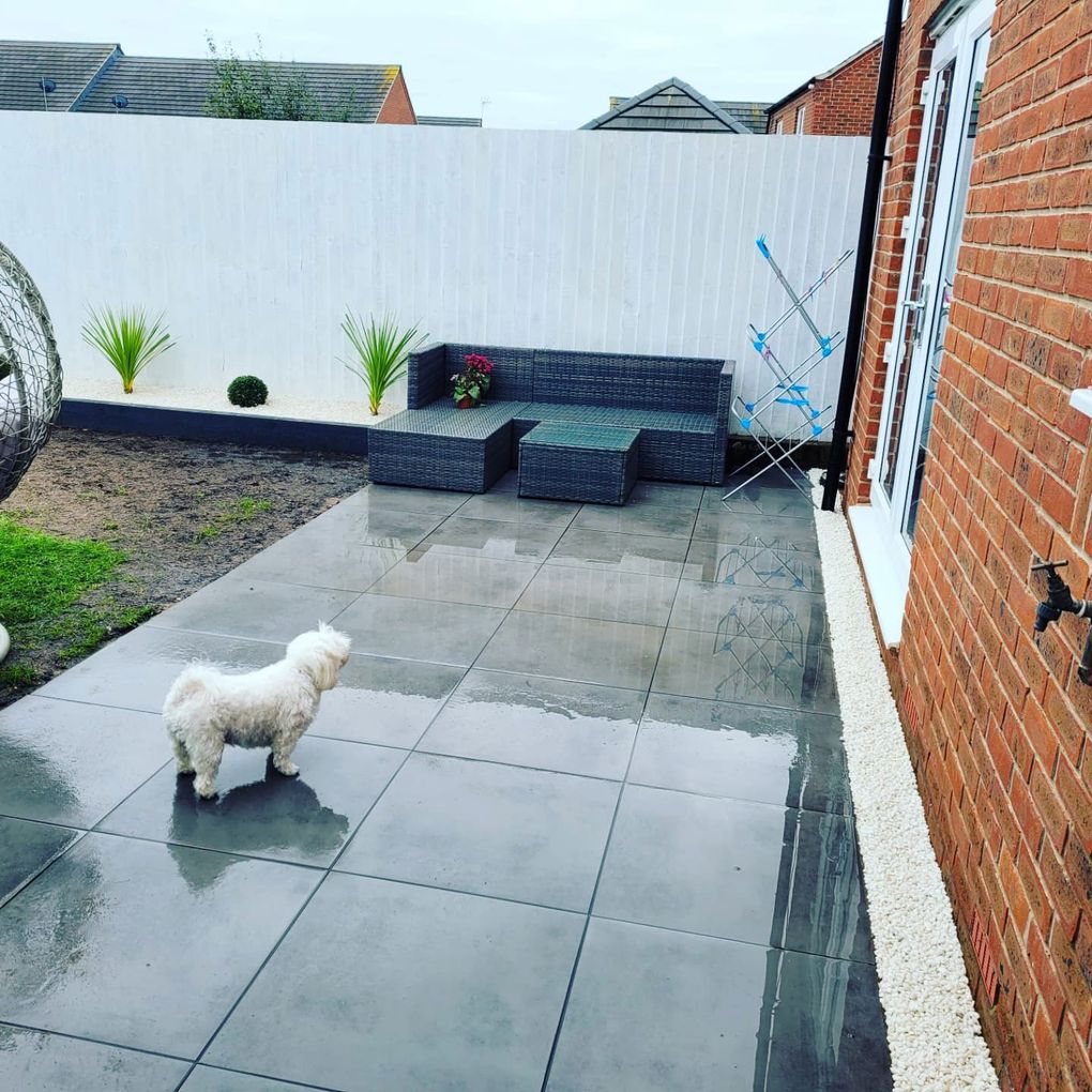 Dark grey porcelain patio with outdoor seating, white gravel edging and a painted fence