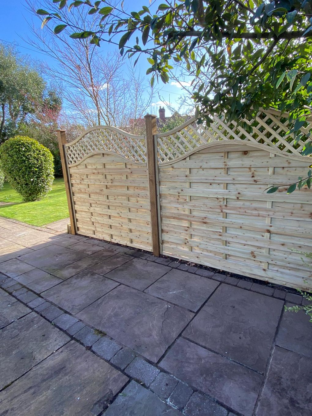 Arched-top timber fence panels with trellis installed alongside a patio