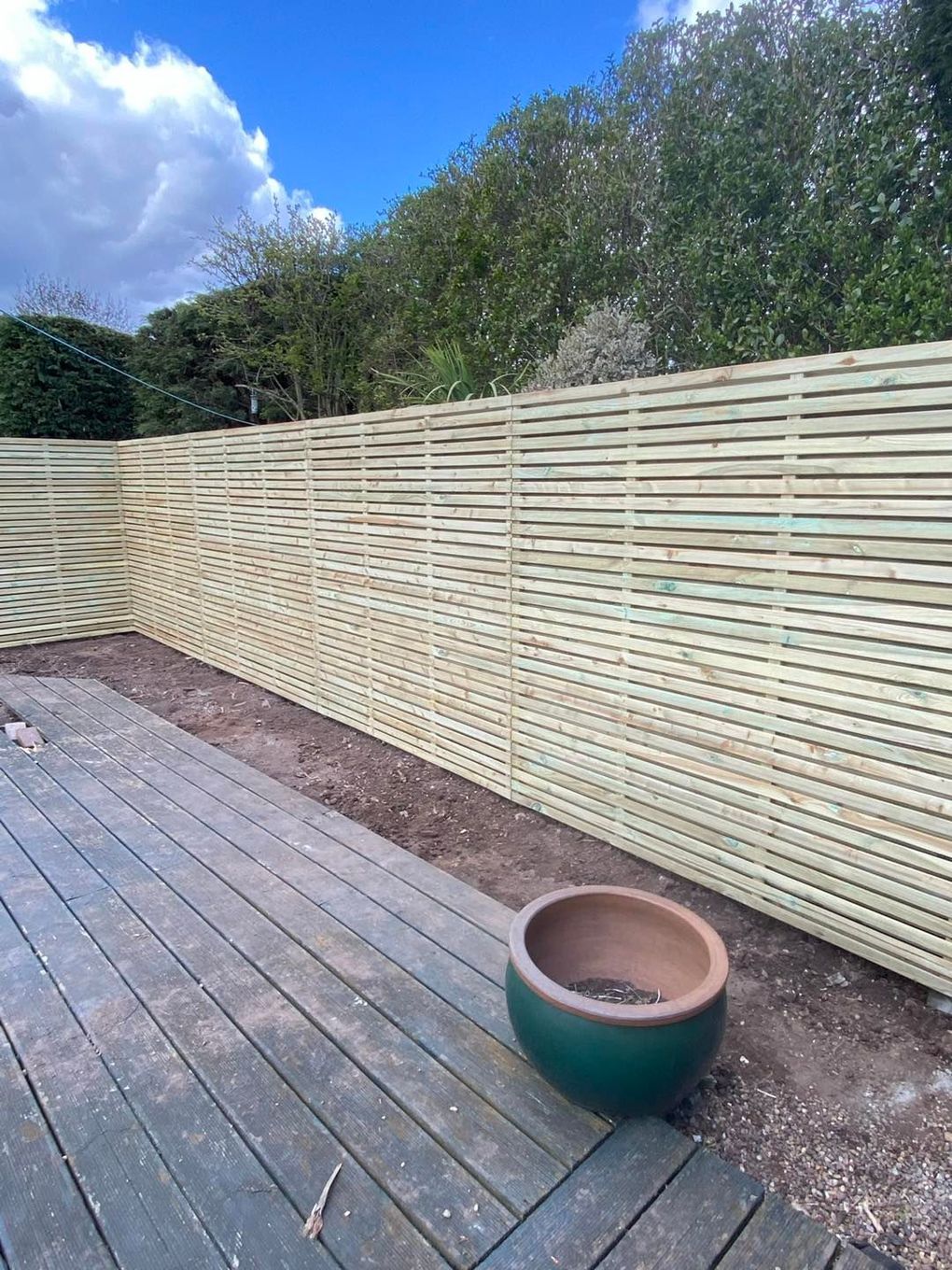Tall slatted timber privacy fence along a garden boundary with trees beyond