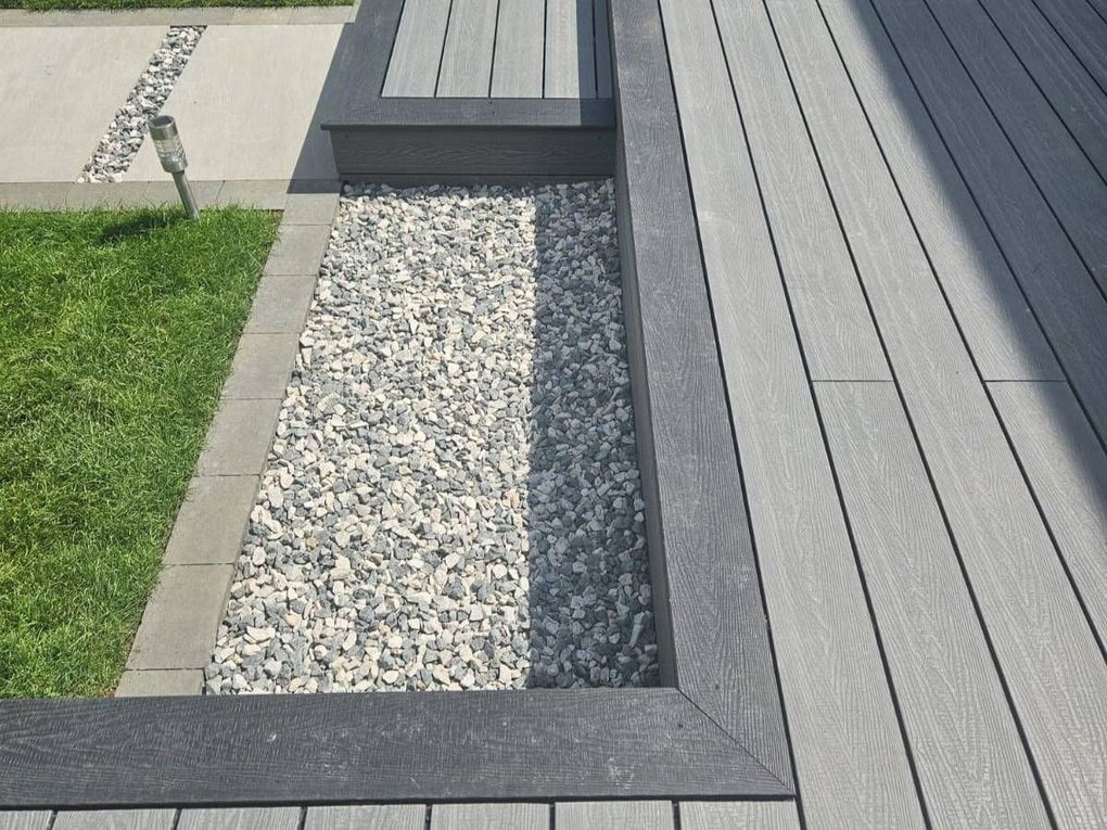 Grey composite decking with a decorative gravel channel beside a lawn in Wyken, Coventry