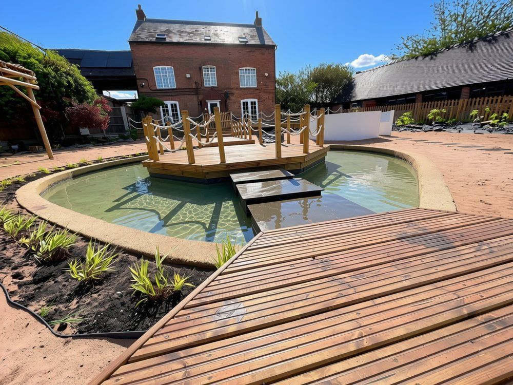 Timber boardwalk leading to stepping stones and a rope-edged island deck in the lagoon, with young ornamental grasses planted along the edge