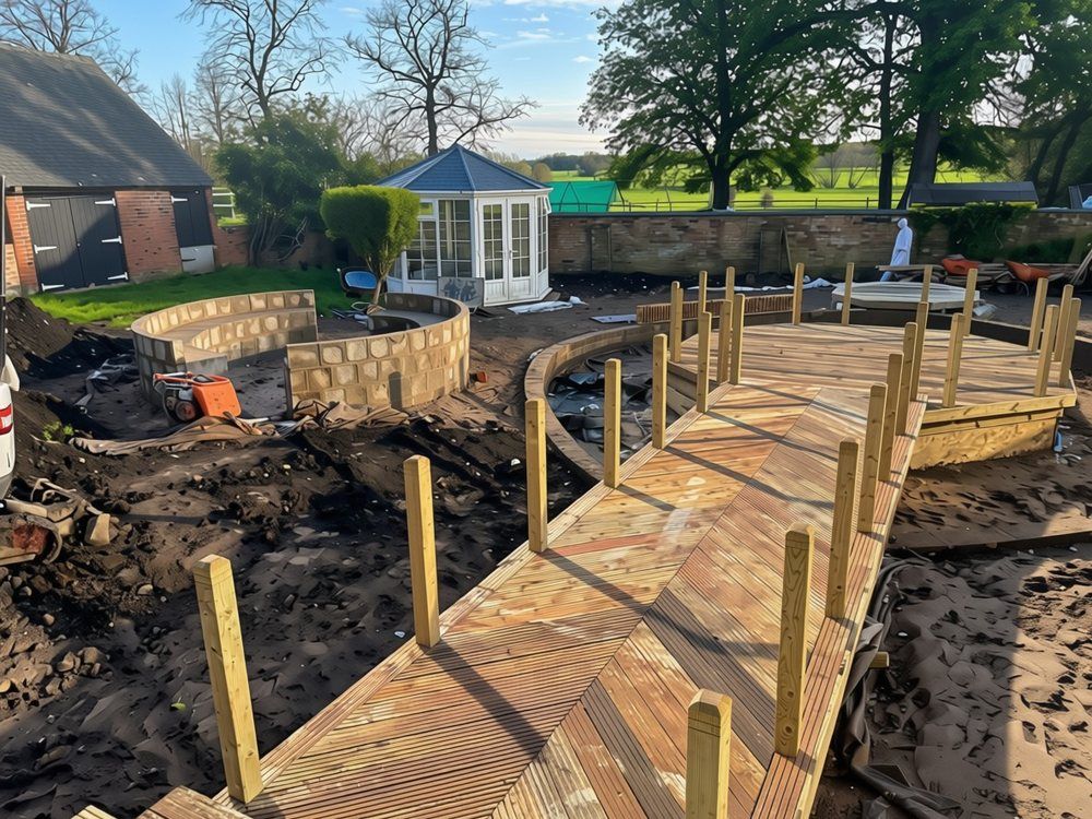 Timber jetty with herringbone deck boards and newel posts leading to an island deck, with curved fire pit seating walls under construction