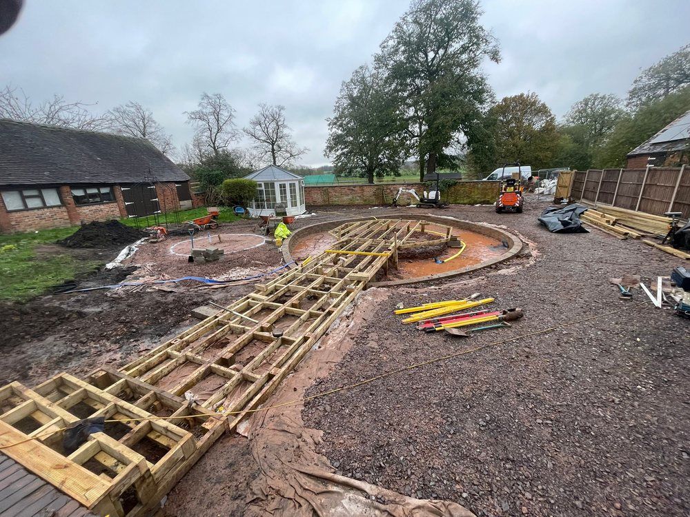 Timber jetty and island deck subframe built across a curved block-walled lagoon, with the fire pit circle marked out alongside