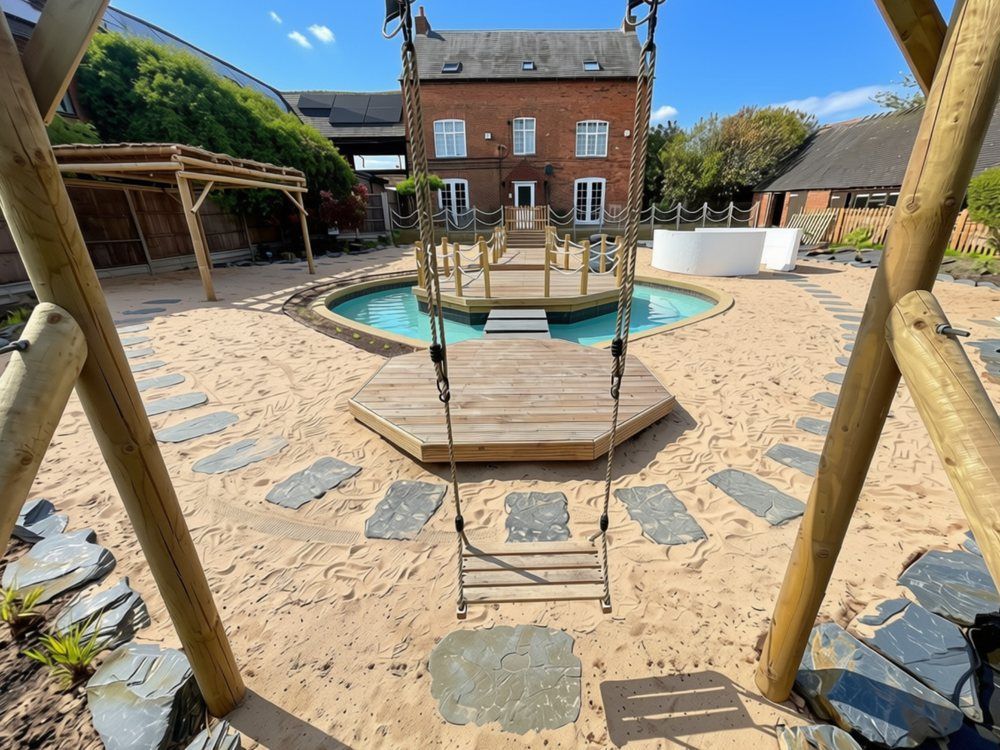Rope swing hanging from a round-pole timber frame, looking across slate stepping stones and sand to a small deck, the lagoon and the farmhouse