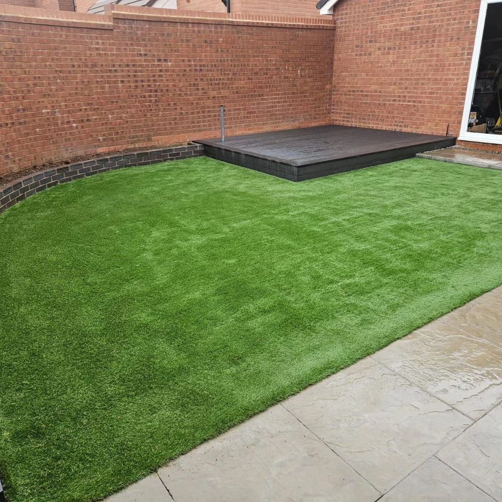 Artificial lawn meeting a curved brick wall and a low composite deck beside a paved path