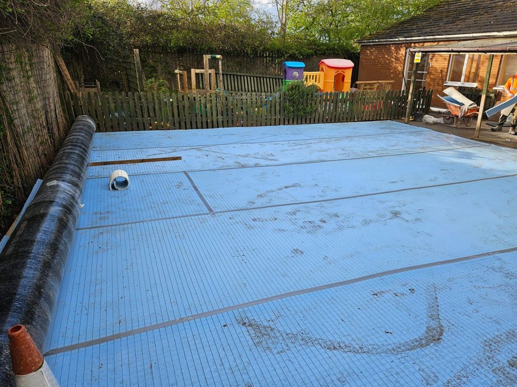 Underlay laid across a garden with a roll of artificial grass ready to go down