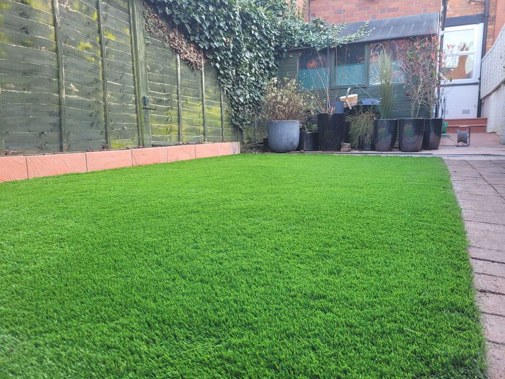 Artificial lawn edged with block paving in front of a patio with potted plants
