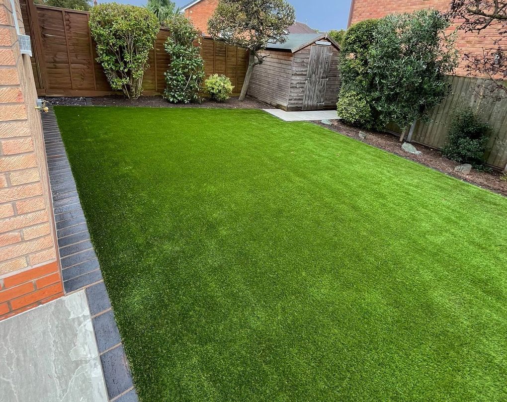 Artificial lawn in a back garden framed by a grey paved border and shrubs