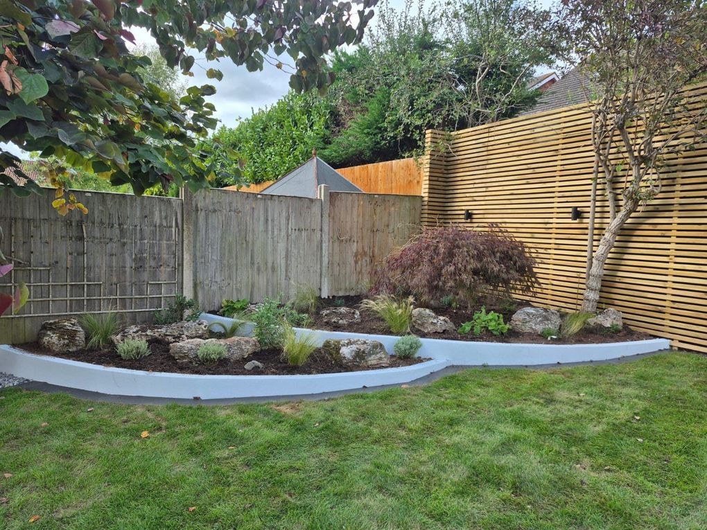 Curved rendered wall planter with rocks and planting beside the lawn, with retained trees and screening behind