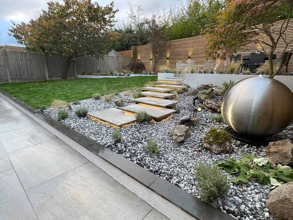 Floating porcelain steps crossing decorative stone and planting towards a raised seating area, with a sphere water feature