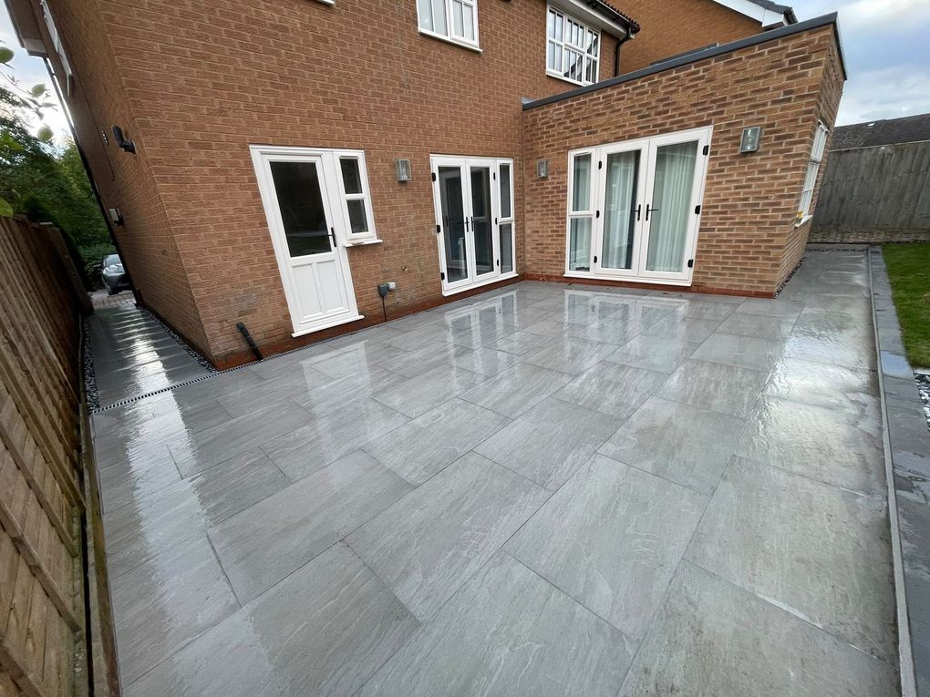 Finished Kandla Grey porcelain patio across the back of a detached brick house