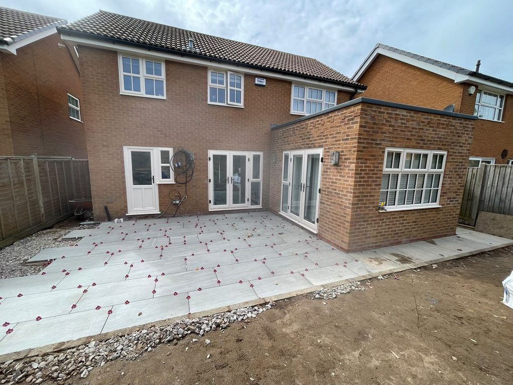 Kandla Grey porcelain slabs being laid across the patio behind a detached brick house