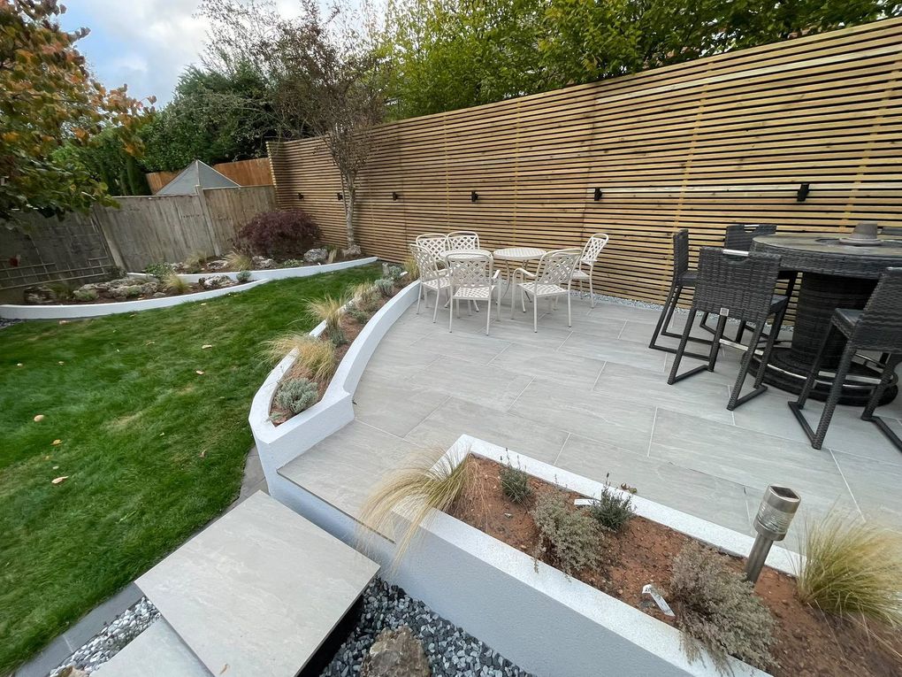 Raised porcelain seating area edged by curved rendered planters with ornamental grasses