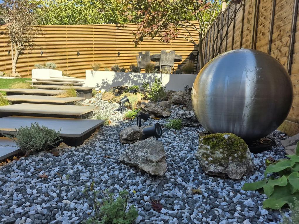 Stainless steel sphere water feature among rocks, gravel and planting beside floating steps