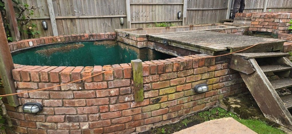 Old raised brick pond with a timber cover and steps in the Galley Common garden before the decking project