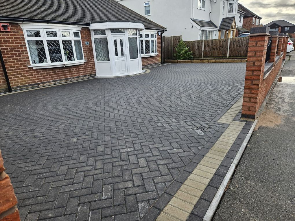 Charcoal herringbone block paving driveway with a buff border in front of a bungalow with brick piers