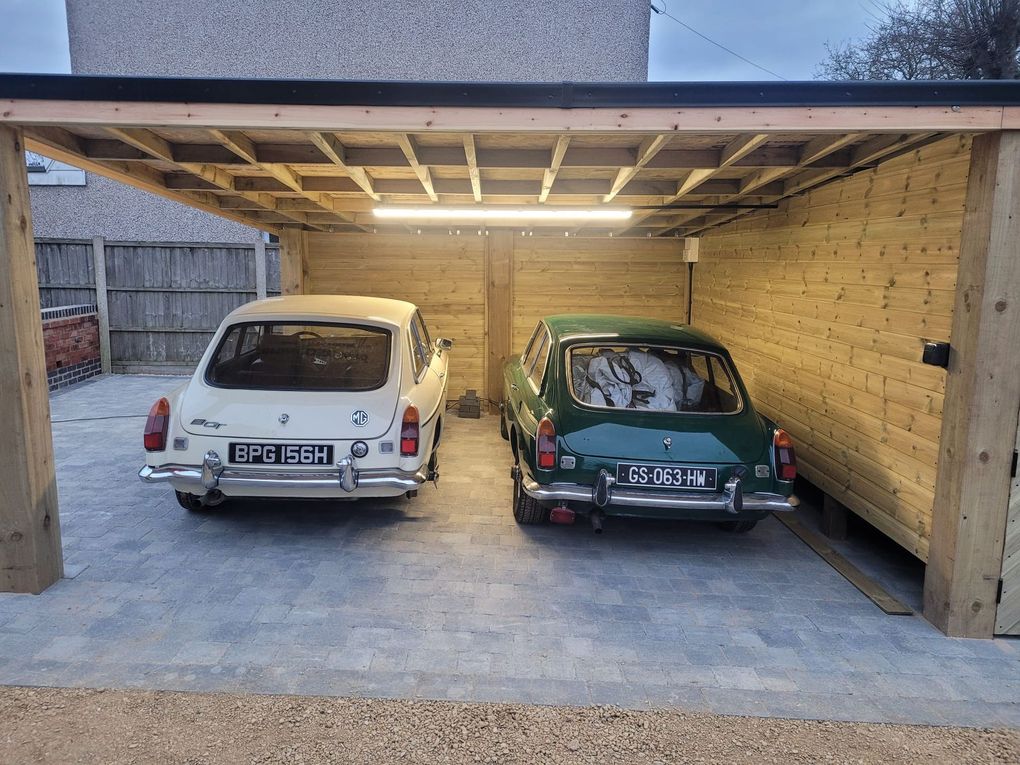 Cobble-effect block paving under a timber carport with two classic cars parked inside