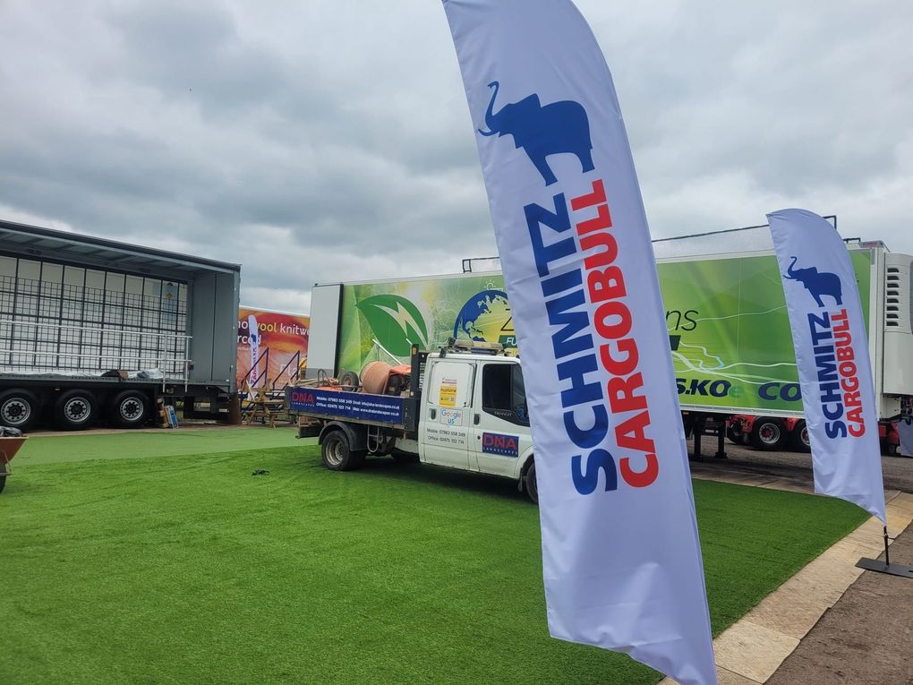Artificial grass laid across an outdoor commercial area with a van and lorry trailers behind