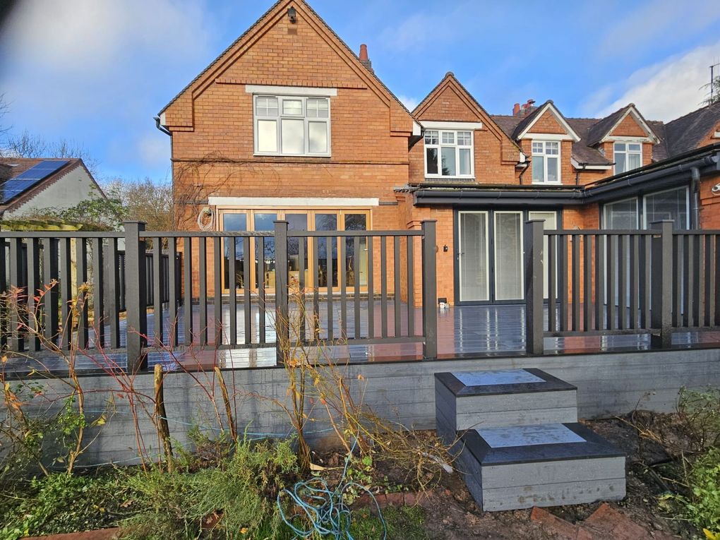 Raised grey composite deck with matching balustrade and steps behind a red-brick house