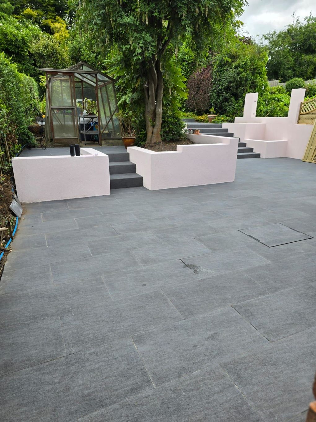 Finished dark porcelain terrace with rendered raised beds and a greenhouse beyond